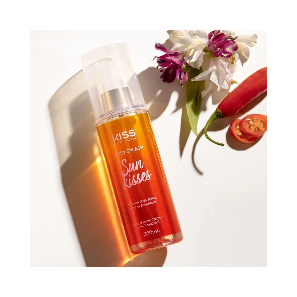 Frasco transparente do Body Splash Kiss New York Sun Kisses 200ml inclinado com flores ao lado